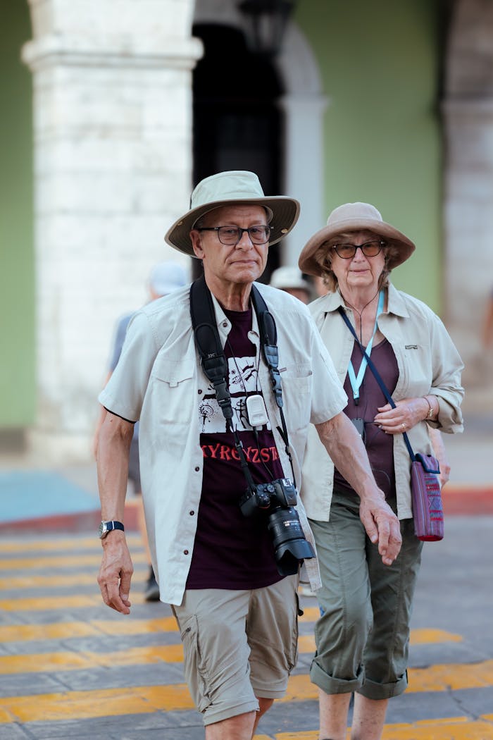 Elderly couple with sun hats and cameras crossing a zebra crossing outdoors.