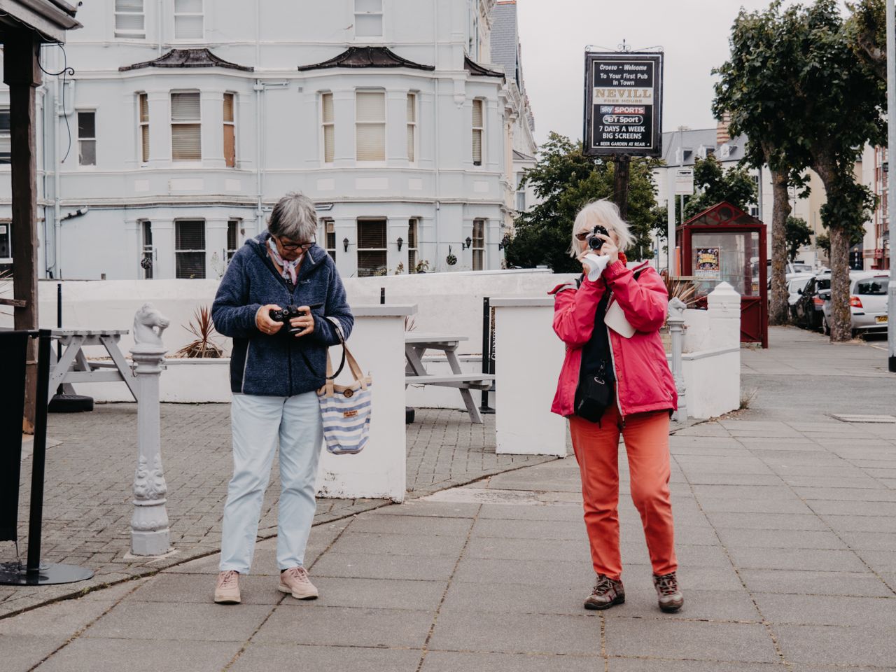 Elderly women capturing city scenes on a sidewalk, showcasing urban exploration.