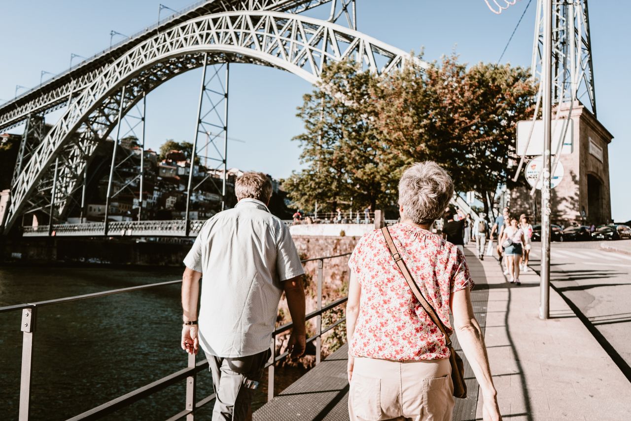 Elderly couple walking near the iconic Dom Luis I Bridge in Porto, Portugal on a sunny day.