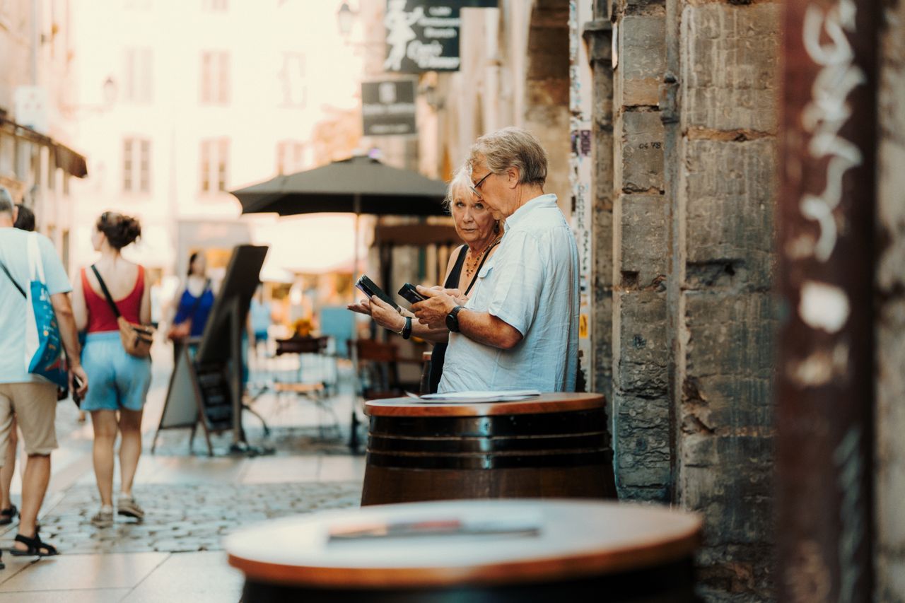 A senior couple examines their surroundings in a quaint European street setting.