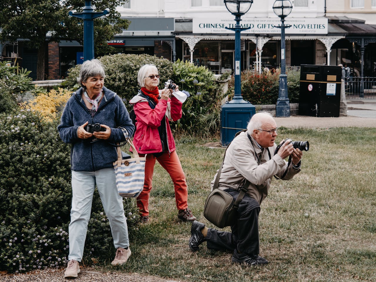 Group of senior tourists taking pictures in an urban park with cameras.